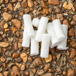 May include: A group of white cotton swabs arranged on a brown and gray gravel surface.