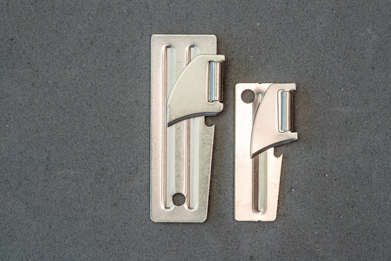 May include: Two silver can openers, one larger than the other, are shown against a gray background. Both openers have a blade and a bottle opener.