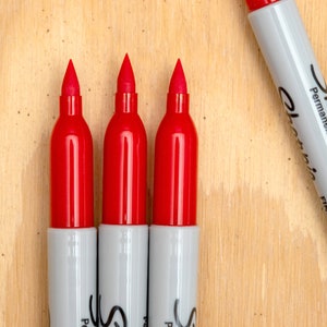 May include: Three red permanent markers with white caps and the text "Sharpie&reg;  Permanent Marker  Fine Point" on the side of one marker.
