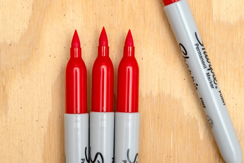 May include: Three red permanent markers with white caps and the text "Sharpie&reg;  Permanent Marker  Fine Point" on the side of one marker.
