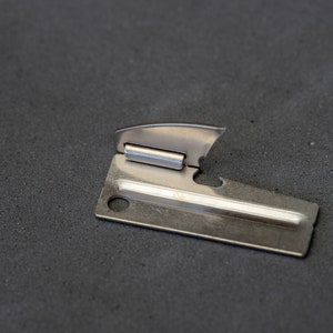 May include: A silver can opener with a small, sharp blade and a handle with a hole for opening cans.