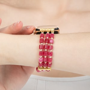 May include: A gold and pink beaded watch band with a gold clasp. The band is made of multiple strands of small, square-shaped beads.