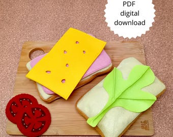 May include: Felt food set featuring a sandwich with yellow cheese, pink filling, and a green leaf, along with two red tomato slices. The items are arranged on a wooden cutting board. The image includes the text "PDF digital download."