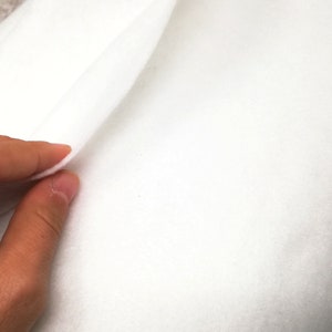 以下が含まれることがあります： 白いフェルト生地を半分に折り畳んで、柔らかな質感を見せます。生地は滑らかで、軽量のようです。