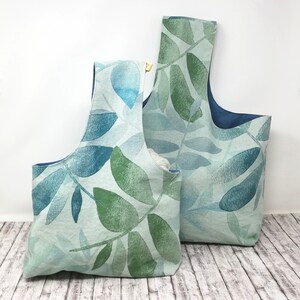May include: Two tote bags with a leaf pattern in shades of blue and green. The bags have a handle and a blue interior. The bags are made of fabric and are designed for carrying items.
