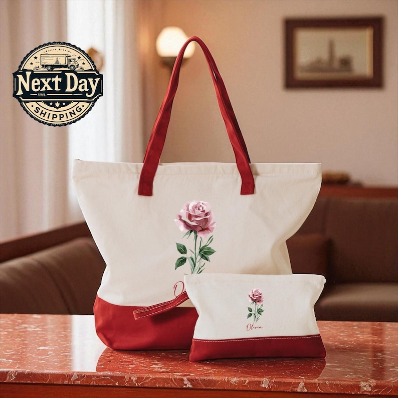 A large white tote bag with a red handle and a smaller white makeup bag with a red handle, both featuring a pink rose design, are displayed on a marble countertop.