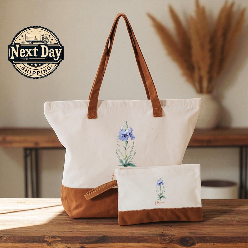 A beige tote bag with a floral design and brown handles, accompanied by a smaller white bag with a similar floral design, both placed on a wooden surface.