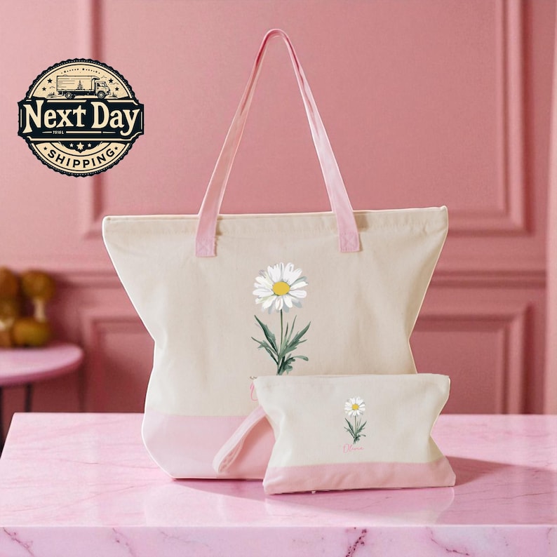 A pink tote bag with a white daisy flower design and a matching pink handle, accompanied by a smaller white bag with a similar flower design, both placed on a pink marble surface.