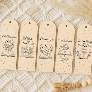 May include: Five beige bookmarks with black illustrations and text. Each bookmark features an open book with botanical designs and German text. The bookmarks are arranged on a textured, off-white surface.