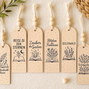 Könnte beinhalten: Set aus sechs Holz-Lesezeichen mit dekorativen Designs und Text. Jedes Lesezeichen zeigt eine einzigartige Illustration eines offenen Buches mit botanischen oder himmlischen Elementen. Die Lesezeichen haben eine natürliche Holzoberfläche und sind mit Holzperlen und Quasten verziert.