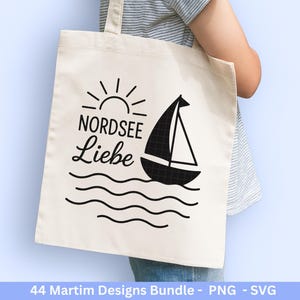 Op de afbeelding: Cr&egrave;mekleurige draagtas met een zwart zeilbootontwerp, de woorden "NORDSEE Liebe" en een zon. De tas wordt door een persoon vastgehouden. De onderkant van de afbeelding heeft de tekst "44 Martim Designs Bundle - PNG - SVG".