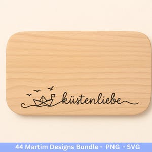 Op de afbeelding: Een lichtgekleurde houten snijplank met afgeronde hoeken. Een zwarte lijntekening van een papieren boot, golven en vogels is te zien. Het woord "k&uuml;stenliebe" is in cursief geschreven.