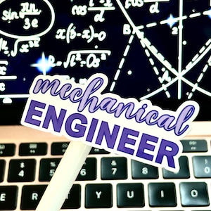 May include: A purple and white sticker with the text "mechanical ENGINEER" on a laptop keyboard. The sticker is on a white pen.