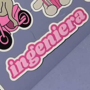May include: A collection of stickers featuring a pink motorcycle, a cartoon dog, and the word "ingeniera" in pink bubble letters with a white outline. The stickers are on a light purple background.