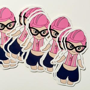 May include: A collection of stickers featuring a cartoon construction worker with pink hair, a pink hard hat, and black glasses. The worker wears a pink and white striped vest, a white shirt, and navy blue shorts. The stickers are on a white background.