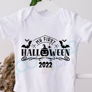 K&ouml;nnte beinhalten: Wei&szlig;er Baby-Strampler mit schwarzem Text "Mein erstes Halloween 2022" mit einem K&uuml;rbis, Flederm&auml;usen und Sternen.