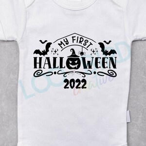 K&ouml;nnte beinhalten: Wei&szlig;er Baby-Strampler mit schwarzem Text, der "My First Halloween 2022" lautet. Der Text ist von Flederm&auml;usen, einem K&uuml;rbis mit Hexenhut und Sternen umgeben.