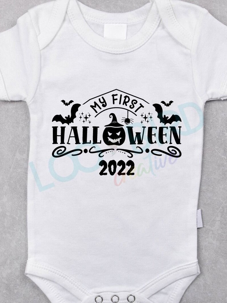 K&ouml;nnte beinhalten: Wei&szlig;er Baby-Strampler mit schwarzem Text, der "My First Halloween 2022" lautet. Der Text ist von Flederm&auml;usen, einem K&uuml;rbis mit Hexenhut und Sternen umgeben.