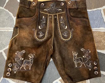 May include: Brown leather shorts with decorative white embroidery featuring deer and floral designs. The shorts have pockets and button details. A traditional garment.
