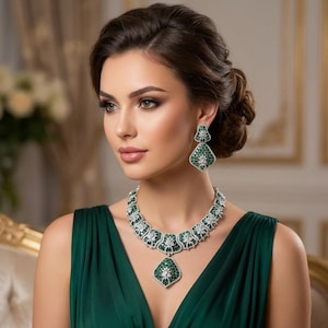 May include: A jewellery set consisting of a necklace and matching drop earrings. The pieces feature deep green stones set in silver-toned metal with clear white accents. The necklace has a central pendant and the earrings are triangular in shape.