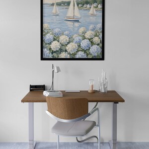 May include: A framed painting of sailboats on the water with white sails, blue water, and white and blue flowers in the foreground. The painting hangs above a wooden desk with a chair.