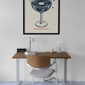 May include: A framed poster with the text "LATE NIGHT VINYL" above a cocktail glass design with a record inside. The text "DRINKS SERVED ON WAX" is below the glass. The poster is on a desk with a chair.