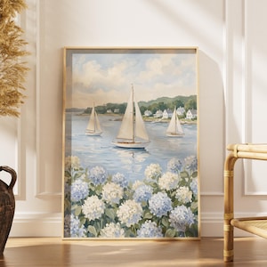 May include: A framed nautical painting depicts sailboats on a serene blue sea, with white and blue hydrangeas in the foreground. The artwork is in a gold frame, creating a coastal theme. The painting is displayed near a vase with dried plants.