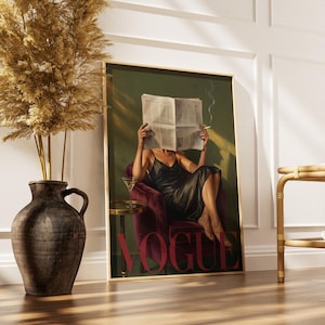 May include: A framed print featuring a woman in a black dress reading a newspaper, with the word "VOGUE" in red. The artwork has a vintage aesthetic, with a martini glass on a side table. A vase with dried plants is in the foreground.