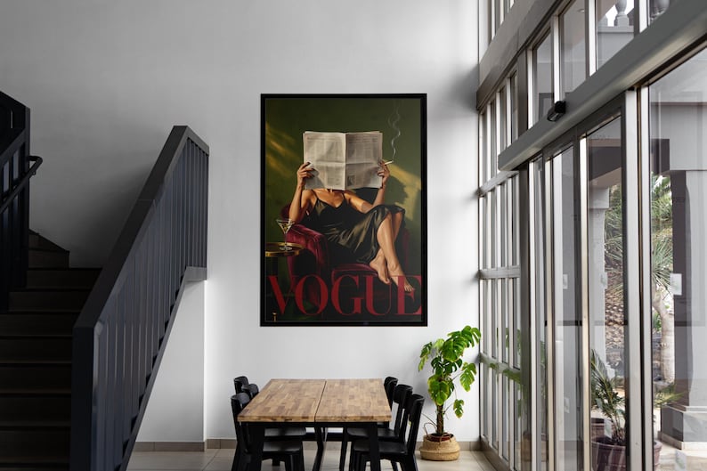 May include: A framed print of a woman reading a newspaper with the word "VOGUE" in red. The woman is seated in a red chair, holding a cigarette. The print is displayed in a modern interior with a wooden table and black chairs.
