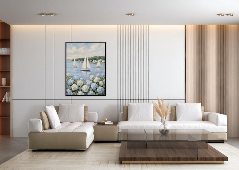 May include: A living room with a modern design. A framed painting of sailboats on the water hangs above a beige sectional sofa. A glass coffee table and a vase with dried plants complete the decor.