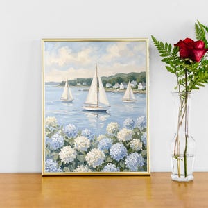May include: A framed painting of sailboats on a blue sea, with white and blue hydrangeas in the foreground. A red rose and greenery are in a clear vase to the right. The painting has a gold frame.