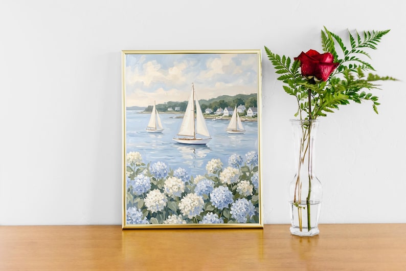 May include: A framed painting of sailboats on a blue sea, with white and blue hydrangeas in the foreground. A red rose and greenery are in a clear vase to the right. The painting has a gold frame.