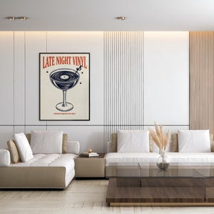 May include: A framed poster with the text "LATE NIGHT VINYL" in red and a graphic of a vinyl record in a cocktail glass. The poster is displayed in a modern living room with a white and beige color scheme.