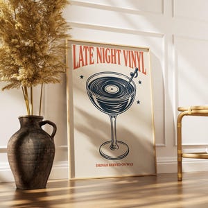May include: A framed poster with the words "LATE NIGHT VINYL" and a graphic of a cocktail glass with a vinyl record inside. The poster also includes the text "DRINKS SERVED ON WAX". A decorative vase with dried plants is to the left.