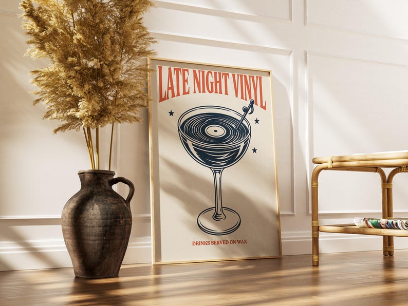 May include: A framed poster with the words "LATE NIGHT VINYL" and a graphic of a cocktail glass with a vinyl record inside. The poster also includes the text "DRINKS SERVED ON WAX". A decorative vase with dried plants is to the left.
