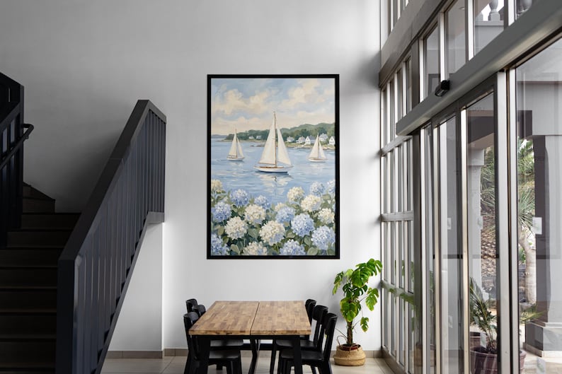 May include: A framed painting of sailboats on a blue sea, with white and blue hydrangeas in the foreground. The artwork is displayed in a modern interior with a wooden table and black chairs.
