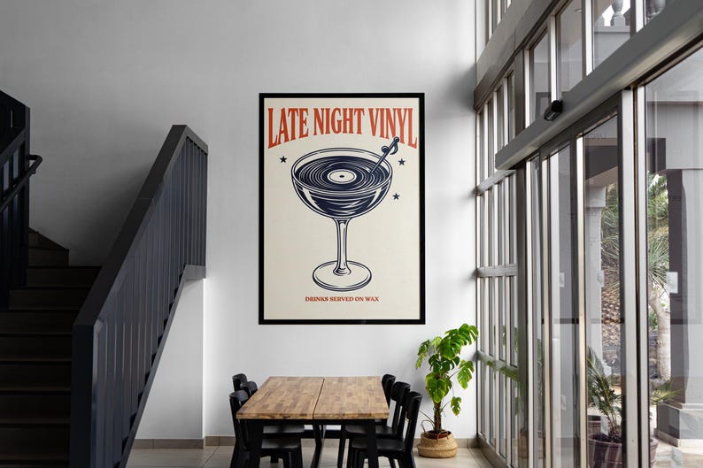 May include: A framed poster with the text "LATE NIGHT VINYL" in red and a graphic of a cocktail glass with a record inside. The poster also includes the text "DRINKS SERVED ON WAX" and is displayed in a room with a table and chairs.