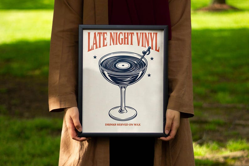 May include: A framed print with a black border featuring a cocktail glass design. The glass is filled with a vinyl record, and the text "LATE NIGHT VINYL" is displayed above. The phrase "DRINKS SERVED ON WAX" is below the glass.