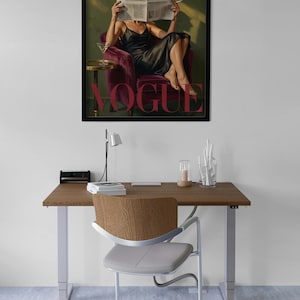 May include: A framed art print featuring a woman in a black dress reading a newspaper, with the word "VOGUE" in pink. The print is displayed above a wooden desk with a chair, lamp, and decorative items.