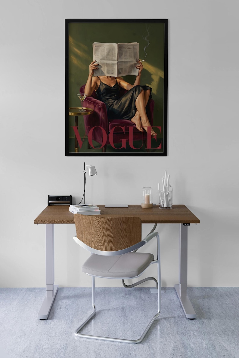May include: A framed art print featuring a woman in a black dress reading a newspaper, with the word "VOGUE" in pink. The print is displayed above a wooden desk with a chair, lamp, and decorative items.