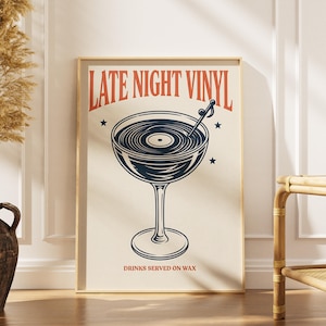 May include: A framed poster with the text "LATE NIGHT VINYL" above a graphic of a cocktail glass filled with a vinyl record design. The poster has a cream background with red and navy blue accents and the text "DRINKS SERVED ON WAX".
