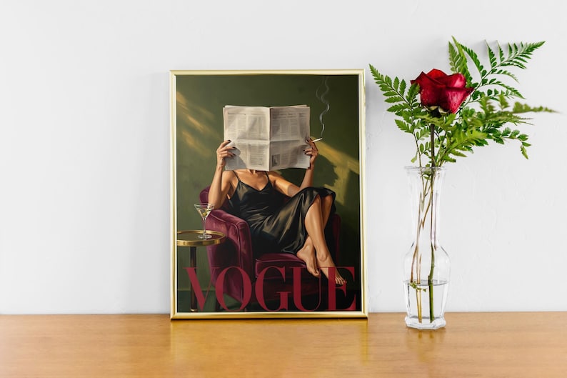 May include: Framed art print featuring a woman in a black dress seated in a burgundy armchair, reading a newspaper. A martini glass sits on a small table. The word "VOGUE" is displayed in red. A red rose in a clear vase is on the right.