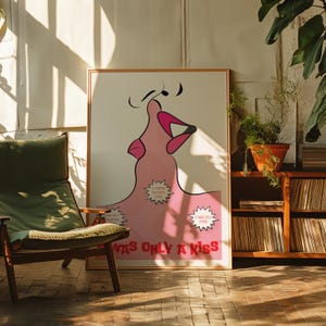 May include: A framed art print with a pink lip design, musical notes, and the text "WAS ONLY A KISS." The artwork includes speech bubbles with phrases like "IT STARTED OUT WITH A KISS." The print is displayed in a room with a green chair and wooden furniture.