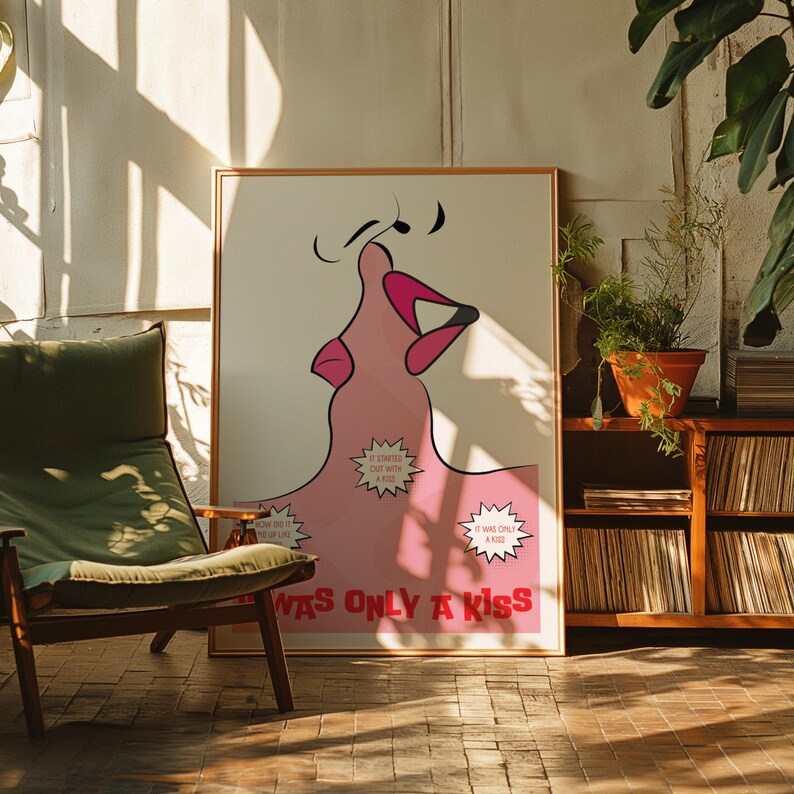 May include: A framed art print with a pink lip design, musical notes, and the text "WAS ONLY A KISS." The artwork includes speech bubbles with phrases like "IT STARTED OUT WITH A KISS." The print is displayed in a room with a green chair and wooden furniture.