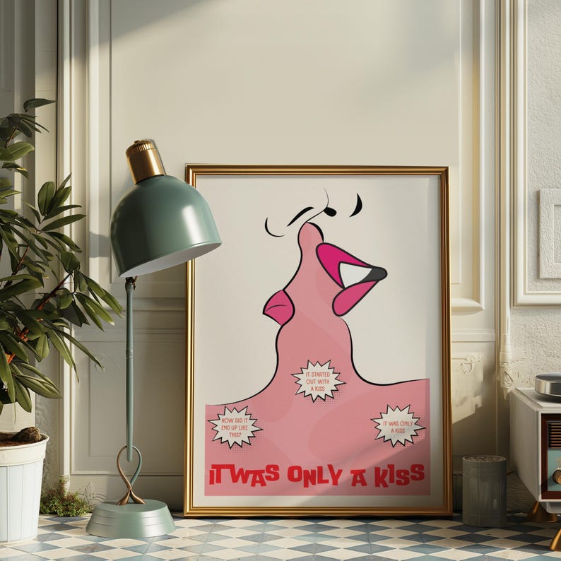 May include: A framed art print with a gold border features a pink illustration of a kiss. The artwork includes the text "IT WAS ONLY A KISS" in red, with speech bubbles. A green lamp and a potted plant are in the foreground.