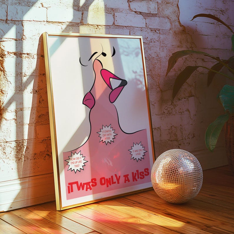 May include: A framed art print with a gold border, featuring a pink illustration of a mouth and the text "IT WAS ONLY A KISS". A disco ball sits on the wooden floor. The artwork leans against a white brick wall.