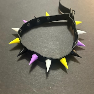 May include: A black leather choker with yellow, white and purple spikes. The choker has a buckle fastening.
