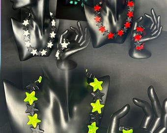 May include: A collection of star-shaped jewelry sets, including necklaces, earrings, and bracelets. The sets feature black and white, red and black, and black and neon green stars. Some stars glow in the dark.