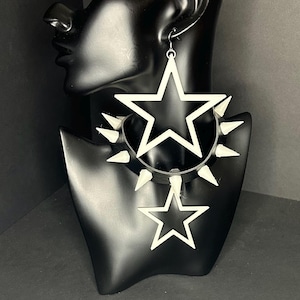 May include: White star-shaped earrings and a matching choker necklace with white spikes. The jewelry is displayed on a black mannequin head. The earrings feature a large star, and the choker has a smaller star pendant.