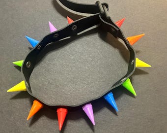 Könnte beinhalten: Ein schwarzer Leder-Choker mit regenbogenfarbenen Spikes. Der Choker hat einen Schnallenverschluss.